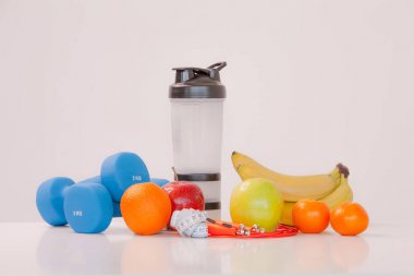 Sağlıklı bir diyet kavramı. Fintes yemek. Spor yaşam tarzı. Halter. Shaker. Portakal. Elma. Muz. meyve suyu. Atlama ipi. Ölçme bant bel. Beyaz bir arka plan üzerinde. Stüdyo çekim.