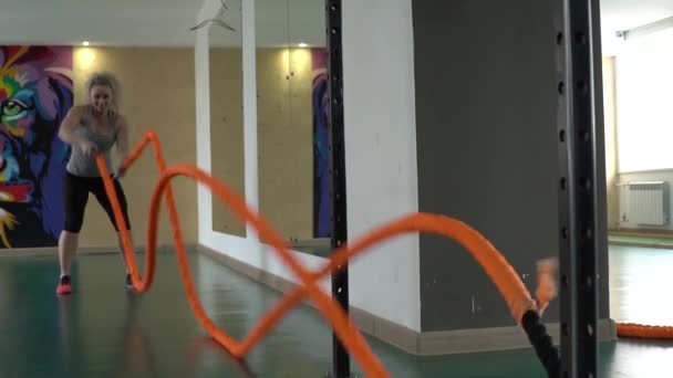 Une jeune femme sportive en tonus travaille avec des cordes de combat dans la salle de gym. Mouvement lent — Video