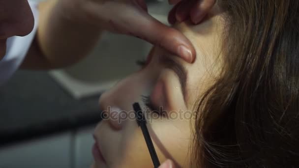 El maquillador pinta rímel en las pestañas de una mujer asiática — Vídeo de stock