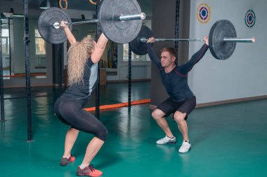 Vücut geliştirme. Genç adam ve kız mekik ile ağırlık yapıyor