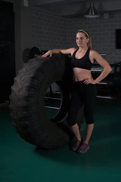 Culturismo de mujer. Mujer de fitness posando cerca del neumático en el gimnasio — Foto de Stock