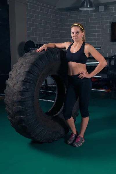 Culturismo de mujer. Mujer de fitness posando cerca del neumático en el gimnasio — Foto de Stock