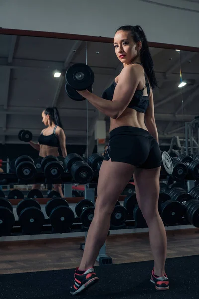 Мускулистая девушка позирует с гантелями в спортзале — стоковое фото