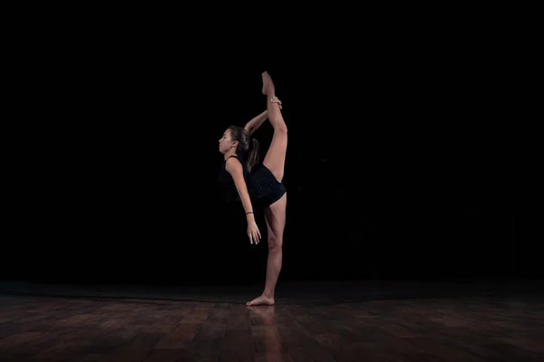 Молода дівчина-гімнастка ізольована на чорному фоні робить гімнастичний ескіз — стокове фото