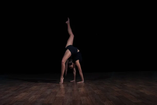 Chica gimnasta haciendo una voltereta sobre un fondo oscuro. Gimnasia deportiva — Foto de Stock