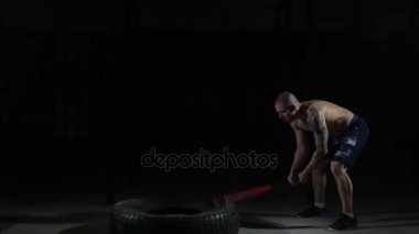 Güçlü kas adam yavaş yavaş üzerinde lastik spor salonunda bir balyoz yener