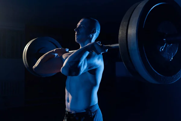 En idrottsman lyfter en skivstång på bröstet i gymmet — Stockfoto