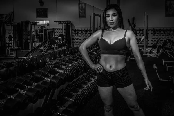 Belle fille modèle de remise en forme posant sur un fond d'haltères dans la salle de gym. Noir et blanc — Photo