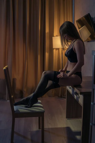 Sexy chica sentada en la mesa y ajustando medias —  Fotos de Stock