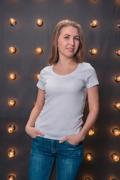 Красивая девушка в классической белой футболке и джинсах на фоне огней — стоковое фото