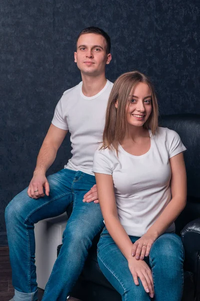 Belle couple fille et mec assis sur une chaise en T-shirts et jeans blancs — Photo