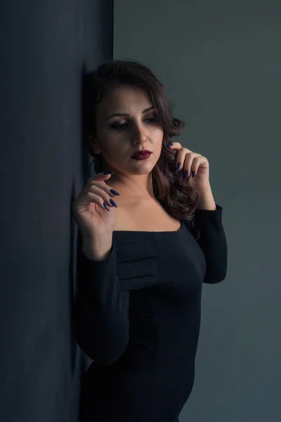 Красивая девушка в сексуальном черном платье позирует, стоя напротив стены — стоковое фото