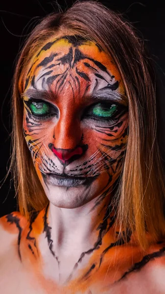 Girl with a painted face of a tiger on a dark background