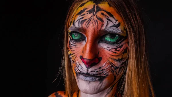 Girl with a painted face of a tiger on a dark background