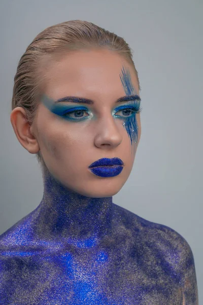 Portrait of a girl in cosmic make-up, a body dotted with sequins on a gray background