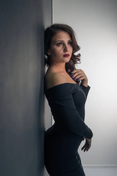 벽에 서 있는 동안 포즈는 섹시 한 검은 드레스에서 아름 다운 여자 — 스톡 사진