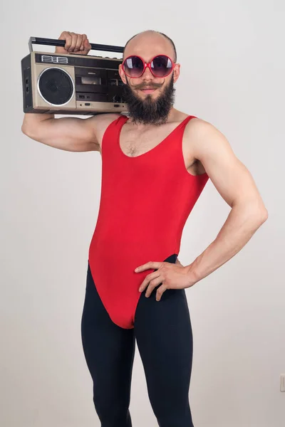 Πορτρέτο ενός αστείου γενειοφόρου άνδρα σε ένα κόκκινο κοστούμι και μαύρο κολάν κρατώντας ένα ρετρό μαγνητόφωνο σε λευκό φόντο — Φωτογραφία Αρχείου