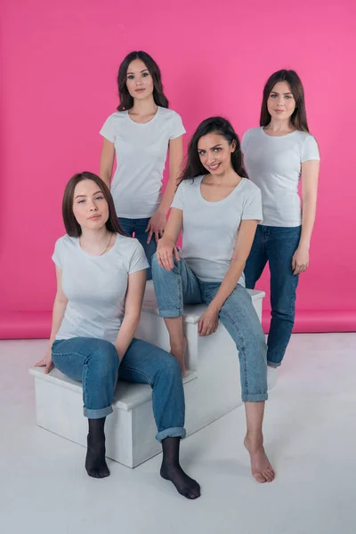 Vier jonge meisjes gekleed in casual stijl pose voor de camera op een roze achtergrond — Stockfoto