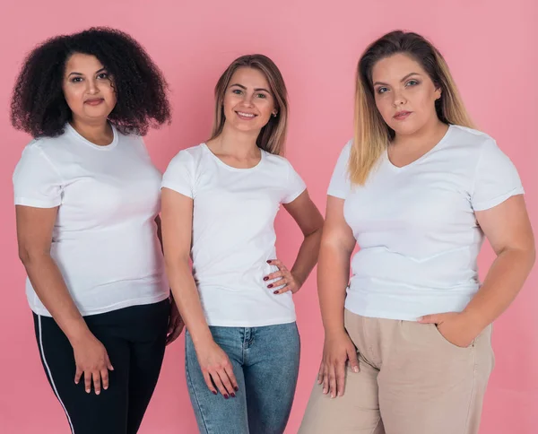 Grupa dziewczyn w czystych białych koszulkach na różowym tle. T-shirt makieta do projektowania na ubrania — Zdjęcie stockowe