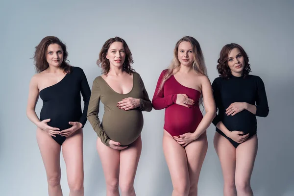 Quattro bella donna incinta in costume da bagno in piedi su uno sfondo bianco . — Foto Stock