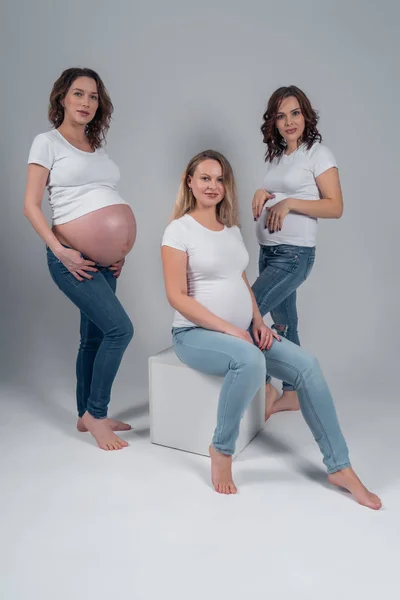 Tři těhotné dívky v bílém tričku a džínách ve studiu. — Stock fotografie