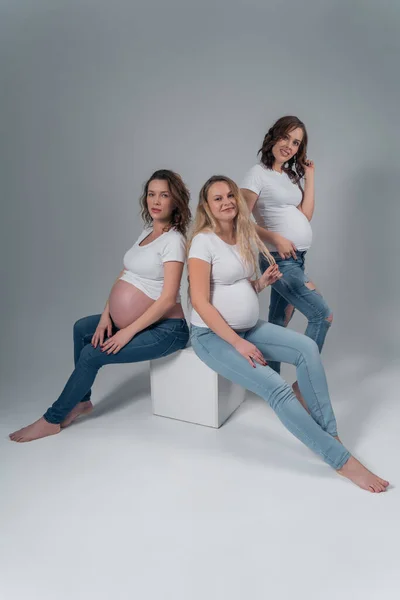 Menina grávida bonita no estúdio no fundo branco em jeans e camisas brancas . — Fotografia de Stock