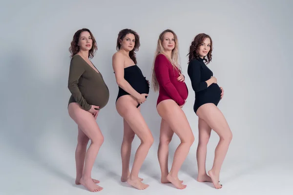 Quatro lindas meninas grávidas em biquínis se destacam em um fundo branco . — Fotografia de Stock
