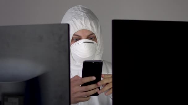 Scienziato in tuta protettiva siede a una scrivania e utilizzare uno smartphone . — Video Stock