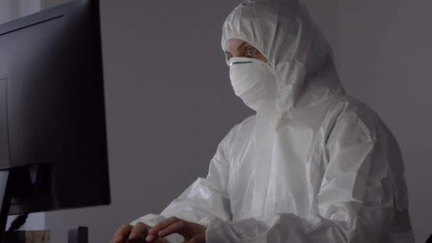 의료용 마스크와 보호용 작업복을 착용하고 있는 과학자가 컴퓨터로 작업 한다. — 비디오