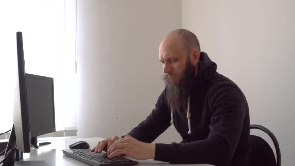 Vousatý plešatý chlap, který píše na klávesnici sedící u stolu — Stock video