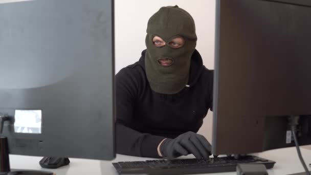 Haker w czarnej bluzie i masce złodzieja włamuje się do pliku komputerowego. — Wideo stockowe