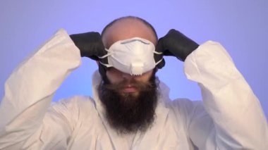 Koruyucu tulumlu bir adam yüzüne tıbbi maske takıyor fermuarlı bir ceket ve kapüşon takıyor.