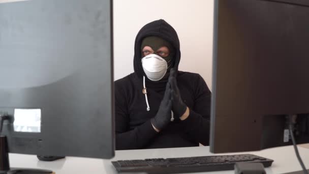 Haker w zakapturzonej kurtce za pomocą komputera przy stole — Wideo stockowe