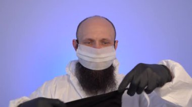 Sakallı bir adam mavi arka planda bir sürü koruyucu maske takar.