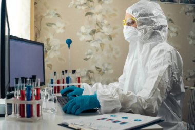 Eldiven giyen bir kadın, koruyucu giysi, yüz kalkanı ve maske takan bir kadın evde çalışıyor. Corona virüsü ya da Covid-19 koruması için.