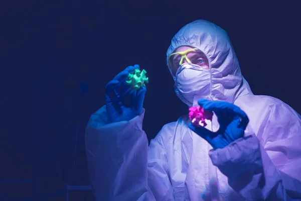 Biolog i skyddsdräkt håller modellen av coronavirus i handen. Stockfoto