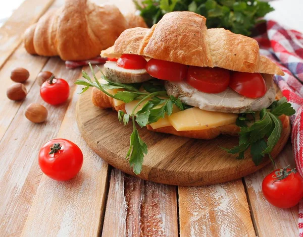 Croissant sandwich med bacon, ost, sallad och tomat på vita träbord. Hälsosamma mellanmål. — Stockfoto