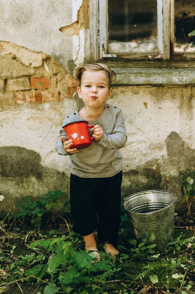 Menino Segurando Caneca Vermelha Balde Fundo Casa Velha — Fotografia de Stock