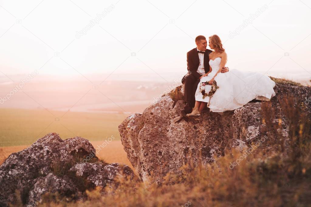 beautiful wedding couple posing sitting on cliff in the mountains