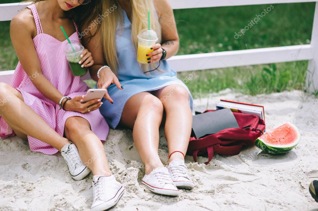 Two happy girls drinking juice and using smartphone 