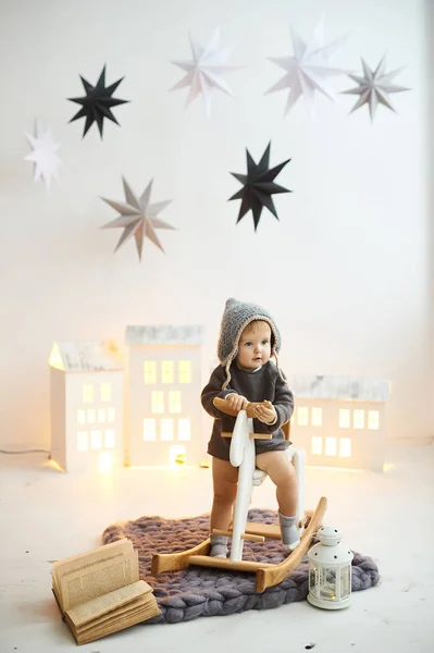 Küçük bir çocuk oyuncak bir evin arka planında tahta bir paten üzerinde oturuyor. — Stok fotoğraf