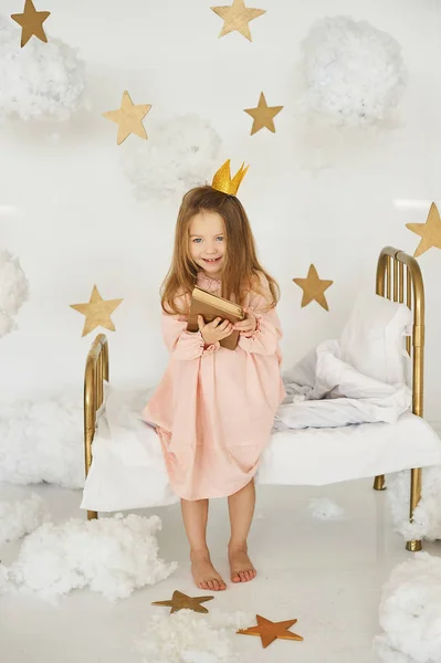 little princess with a magic wand on a bed in a cloud on a white background