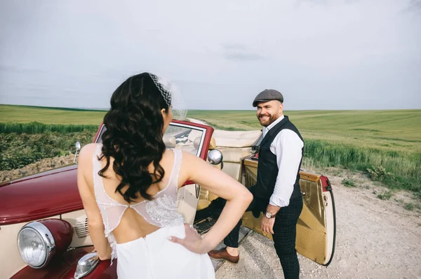 Elegante pareja de boda, novia, novio en un campo verde cerca de retr —  Fotos de Stock