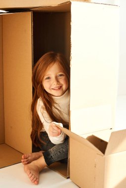 Yeni evindeki karton kutuların içinde küçük bir kız, beyaz bir sırt çantasında.