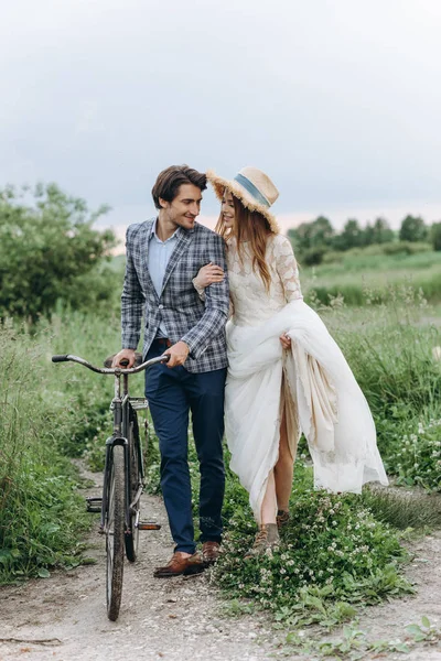 Casal jovem bonita noiva e noivo andando em um campo com um — Fotografia de Stock