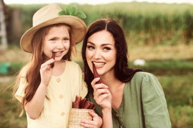 Güzel, genç, beyaz bir anne ve bir sepet çilekli keten bir elbise içinde kızı yeni bir mahsul topluyor ve yeşil alanda eğleniyor.