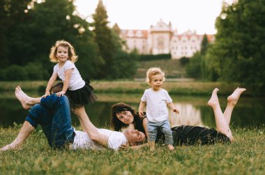 Yakışıklı genç baba ve güzel anne güneşli yaz doğasında sevimli küçük çocuklarıyla oynuyorlar.