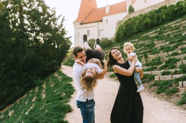 Yakışıklı genç baba ve güzel anne güneşli yaz doğasında sevimli küçük çocuklarıyla oynuyorlar.