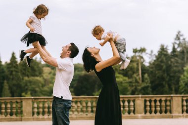 Yakışıklı genç baba ve güzel anne güneşli yaz doğasında sevimli küçük çocuklarıyla oynuyorlar.