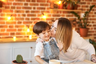 Genç ve güzel bir aile güneşli mutfakta eğleniyor ve yemek pişiriyor.